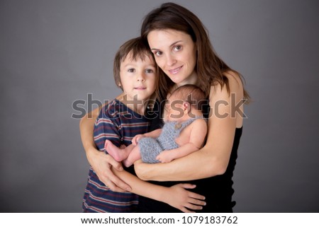 Family picture of two boys and their mom, kissing and hugging newborn baby at gray background, tender, care, love. Portrait of woman and children, happiness concept, isolated image