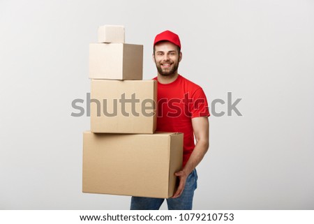 Delivery Concept: Handsome delivery man hold pile cardboard boxes on grey background.