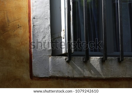 Part of a window in a french mediterranean street. Yellow painted wall. Grey metallic rails to protect the opening. Shadows of the grid reflected on the house facade. Abstract architectural image. 