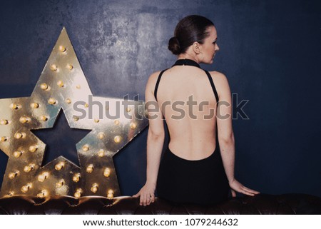 beautiful girl in a simple evening dress with a deep cut on her back poses around the scenery in the form of a star with burning lamps. 