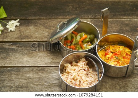 Antique stainless steel food carrier (Tiffin food container) and spoon on wood background. Set of food. Brown rice, Spicy salad long eggplant, carrot and Omelette (Omelet). Copy space. Simple life. Royalty-Free Stock Photo #1079284151