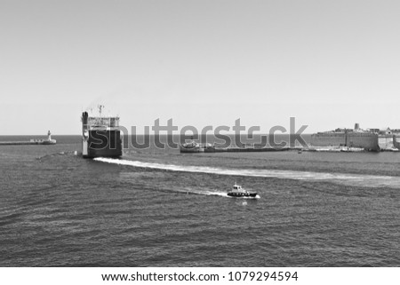 Cargo ship leaves the harbor of Valletta. Lighthouses indicate the entrance to the ports of Malta. Black and white picture