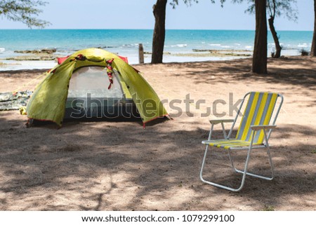 While camping, travellers set their yellow tent and folded chair on the beach by the sea for their relaxation and refresh during holidays