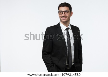 Half-length picture of handsome Caucasian businessman isolated on gray background wearing black suit and eyeglasses looking aside with happy smile, looking relaxed and full of ideas and ambitions