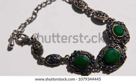 Silver bracelet with green, blue, red stones on a light background. Macro photography. Defocusing
