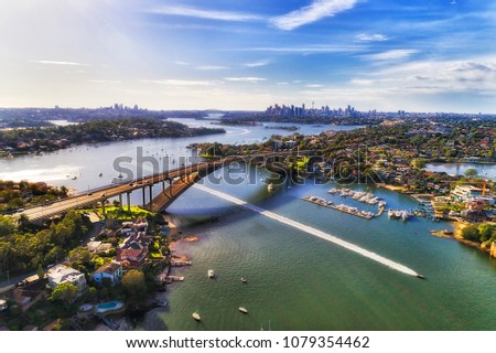 Colourful aerial view over Parramatta river and Gladesville bridge on Victoria road towards Sydney city CBD skyline. Speed boat beats the city traffic on open river water.