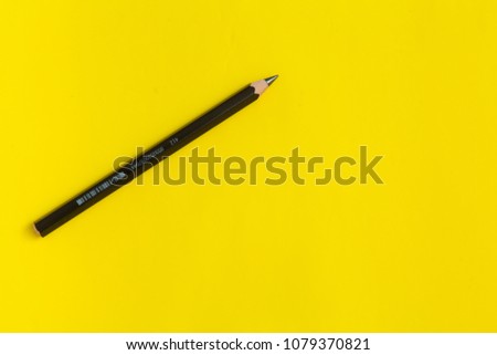 Black pencil on a yellow background, top view