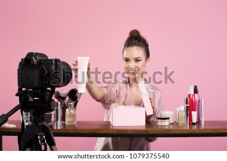 Famous blogger. Cheerful female vlogger is showing cosmetics products while recording video and giving advices for her beauty blog. Focus on digital camera Royalty-Free Stock Photo #1079375540