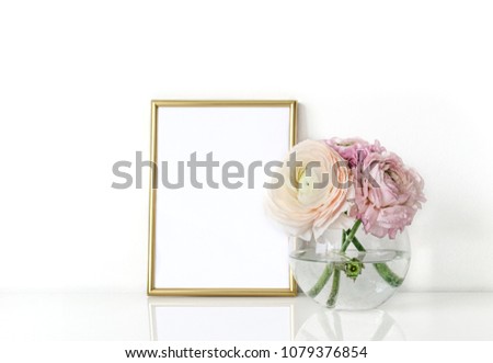 Ranunculus in a vase with a frame for the presentation of works and accessories. Everything is on the table in the interior.Mock-up for displaying works.