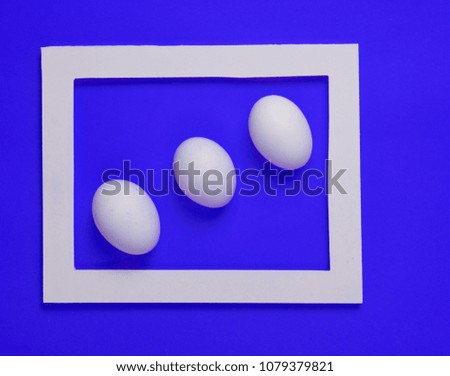Three  chicken eggs in a white frame on a blue background. Minimalist trend.
