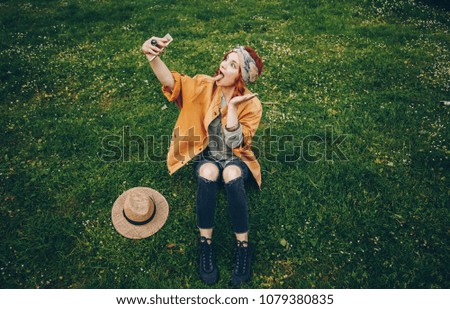 beautiful young woman taking selfie picture outdoors. hippie fashion blogger on vacation, taking self portrait with smartphone. street style, music festival portrait of authentic and fun young girl.