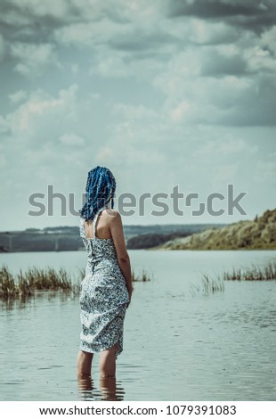 The girl in the dress is knee-deep in the river and looks at the horizon.