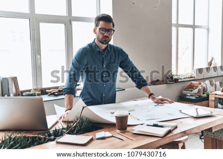 Successful professional. Handsome young man using blueprint while working in the creative working space         