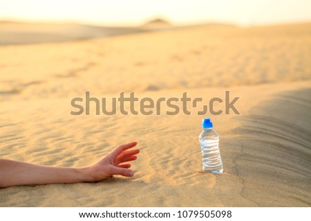Hand try to catch the bottle of water on sand desert in hot temperature. Concept of to die of thirst. Royalty-Free Stock Photo #1079505098
