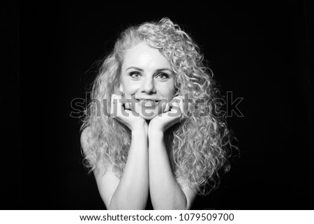 Close up studio portrait of a pretty curly blonde woman, looking at the camera, resting head on hands, against plain studio background