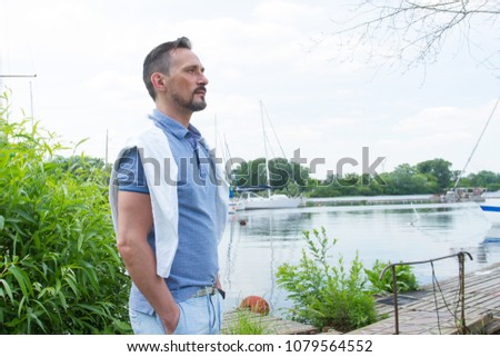 Handsome yachtsman standing on river pier. Man looking into far on his yacht. Young businessman with his yacht in marina. Royalty-Free Stock Photo #1079564552