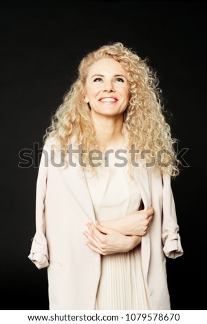 Close up studio portrait of a pretty curly blonde woman, wearing light dress and a coat, laughing and looking up, against plain studio background