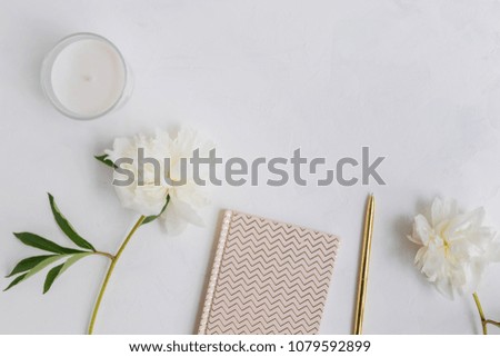 Flat lay desk with white peonies, gold notebook and accessories on light background
