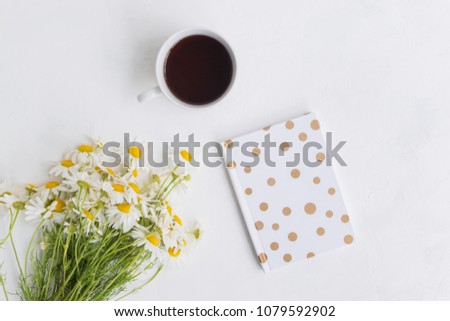 Flat lay desk with white daisies, notebook and cup with tea on light background
