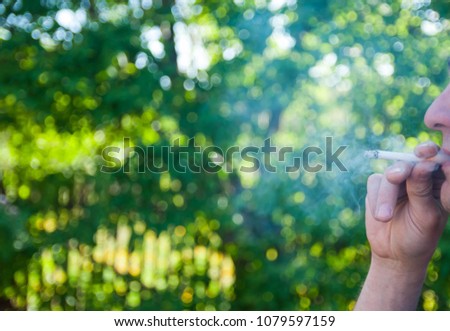 Unidentifiable caucasian male smoking a cigarette at sundown, green blurry background.