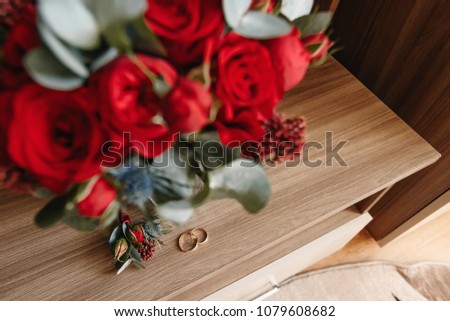 Beautiful picture with wedding rings lie on a wooden surface against the background of a bouquet of flowers