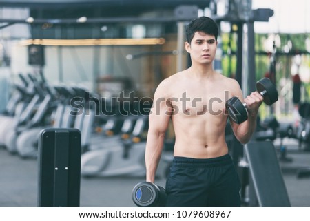 Shirtless young muscular man lift dumbbells in gym. bodybuilder male working out in fitness center.