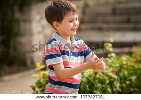 Happy cute Caucasian kid playing with water fountain in the public park.