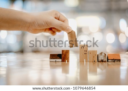 Hand choosing mini wood house model from model and row of coin money on wood table, selective focus, Planning to buy property