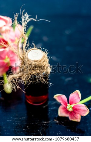 Red colored Ayurvedic and floral essence of Rangoon creeper or Chinese Honeysuckle or Madhumalti in a transparent bottle on wooden surface used in beverages for flavoring and in medicines also.;
