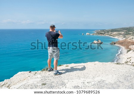 Man near sea making photo with his mobile phone camera.Young man standing on top of cliff in Cyprus, Mediterranean Sea. Travel, vacation concept. Copyplace, place for text