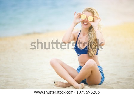 Young attractive woman covering her eyes with lemon slices. Cheerful girl on the beach