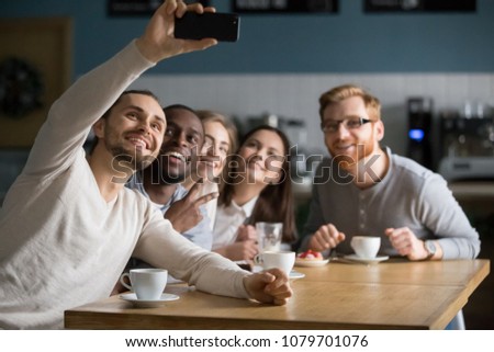 Group selfie concept, diverse millennial friends taking picture on cellphone in cafe, multiracial young people making photo, shooting video on smartphone camera sitting together at coffee shop table