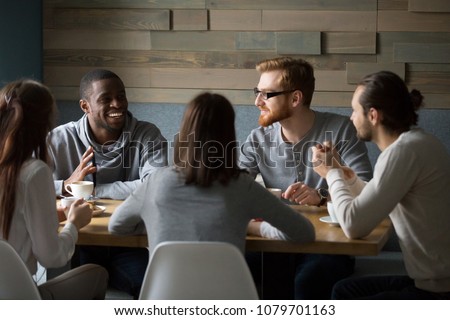 Multiracial young friends talking drinking coffee together sitting at cafe table, african man telling joke while diverse millennial smiling people enjoying listening having fun at coffeehouse meeting Royalty-Free Stock Photo #1079701163