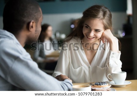 Happy interracial couple flirting talking sitting at cafe table, african man holding hand of smiling caucasian woman having fun drinking coffee together at meeting, biracial lovers on date concept Royalty-Free Stock Photo #1079701283