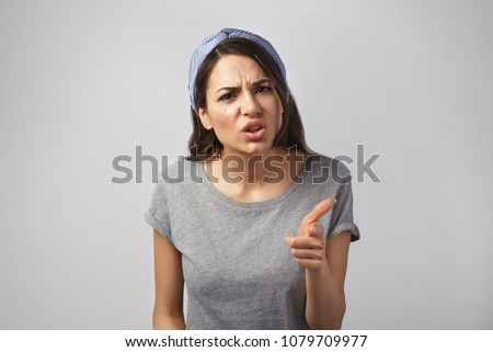 It's your fault. Studio shot of disappointed angry young brunette woman frowning wearing headscarf and gray t-shirt, pointing index finger at camera, being mad, blaming all her failures on you Royalty-Free Stock Photo #1079709977