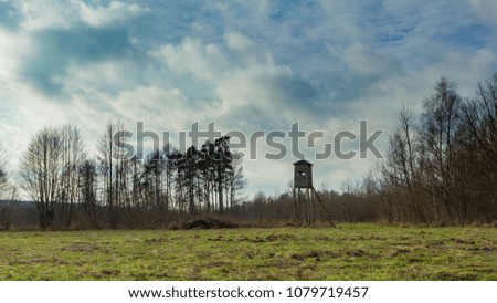 Meadow landscape with raised hide and trees under beautiful cloudy sky.