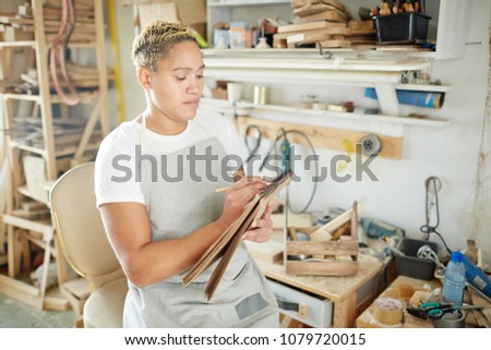 Young African-american woman making working notes or sketching in notepad during work