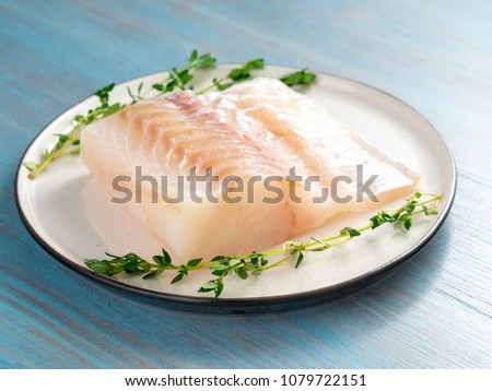 piece of raw cod fish fillet on plate on blue wooden table, side view