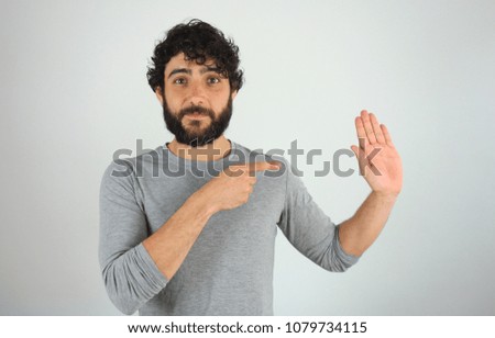 Handsome brunette man with beard and curly hair showing direction and pointing with finger. Studio portrait over gray background.