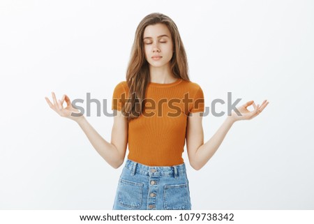 Keeping mind healthy. Calm good-looking stylish woman with blond hair, closing eyes and standing relaxed over gray background with spread zen gesture, meditating or practicing yoga to stay positive