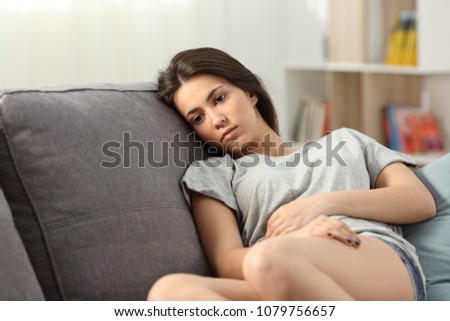 Distracted teen looking away sitting on a couch in the living room at home Royalty-Free Stock Photo #1079756657