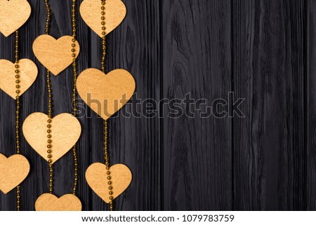 Flat lay border of golden hearts and beads. Festive decor on a black wooden background. View from above.