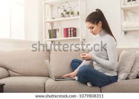 Happy woman shopping online with credit card and laptop, sitting on couch, making order with computer, copy space