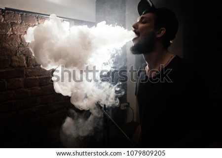 Young man exhales smoke from hookah. Highlighted smoke.
