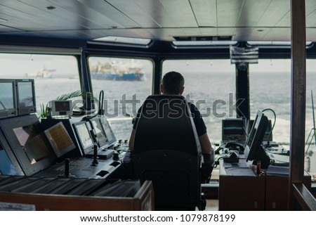 Deck navigation officer on the navigation bridge. He looks to sea. Watchkeeping, collision prevention at sea. COLREG Royalty-Free Stock Photo #1079878199