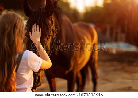 Young blonde girl stroking a brown horse. Royalty-Free Stock Photo #1079896616