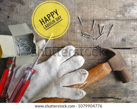 Concept of gloves, hammer, screwdriver, nails, on wooden background with word HAPPY LABOUR DAY.