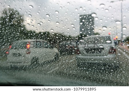Blured background with rains drop on glass and cars on the road, Road view through car window blurry with heavy rain, Driving in rain, rainy weather. Water drop rain on road blur background. 