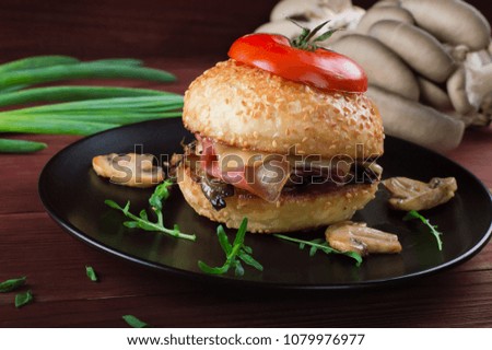 Burger with fried mushrooms, ham, onions and cheese on rustic background.