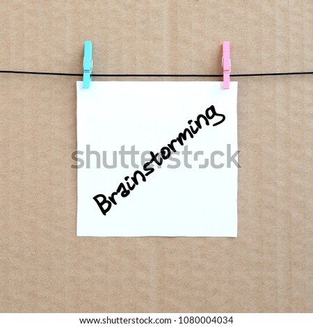 Brainstorming. Note is written on a white sticker that hangs with a clothespin on a rope on a background of brown cardboard